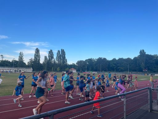 Groupe de coureurs s'exerçant sur une piste, ciel bleu et arbres en arrière-plan.